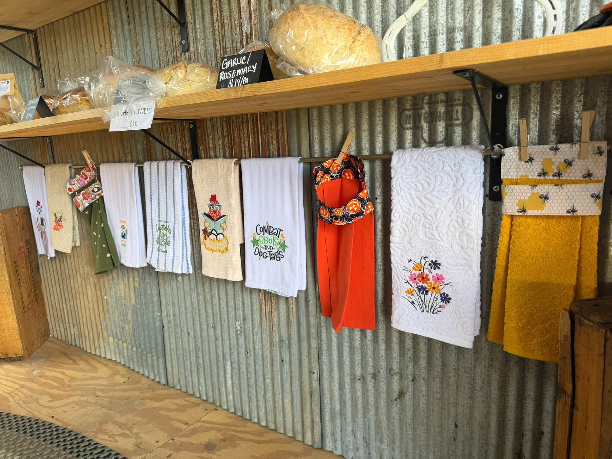 Embroidered kitchen towels and aprons hanging against corrugated metal